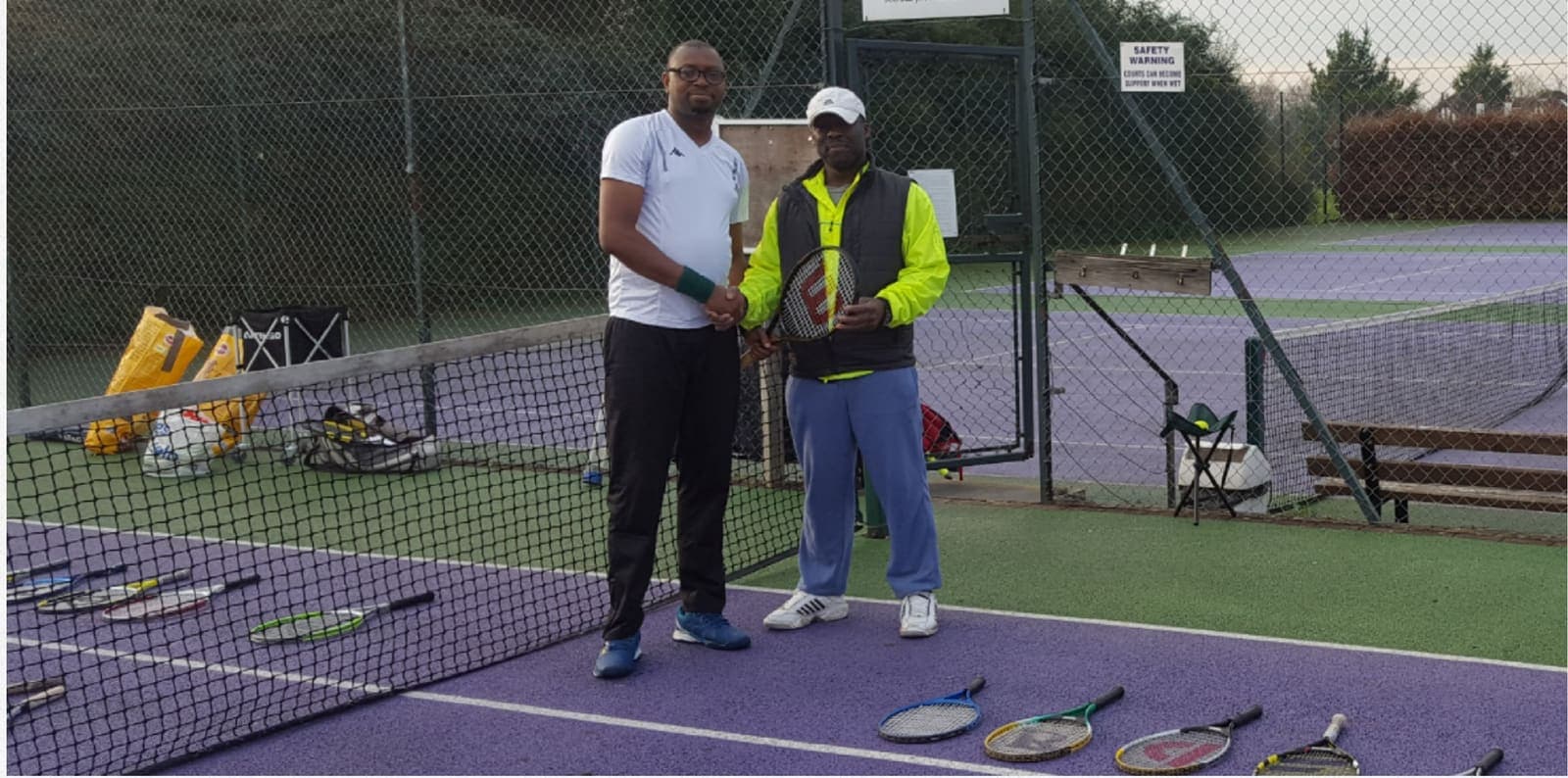 Two people shaking hands on court beside a row of donated racquets in Dar es Salaam