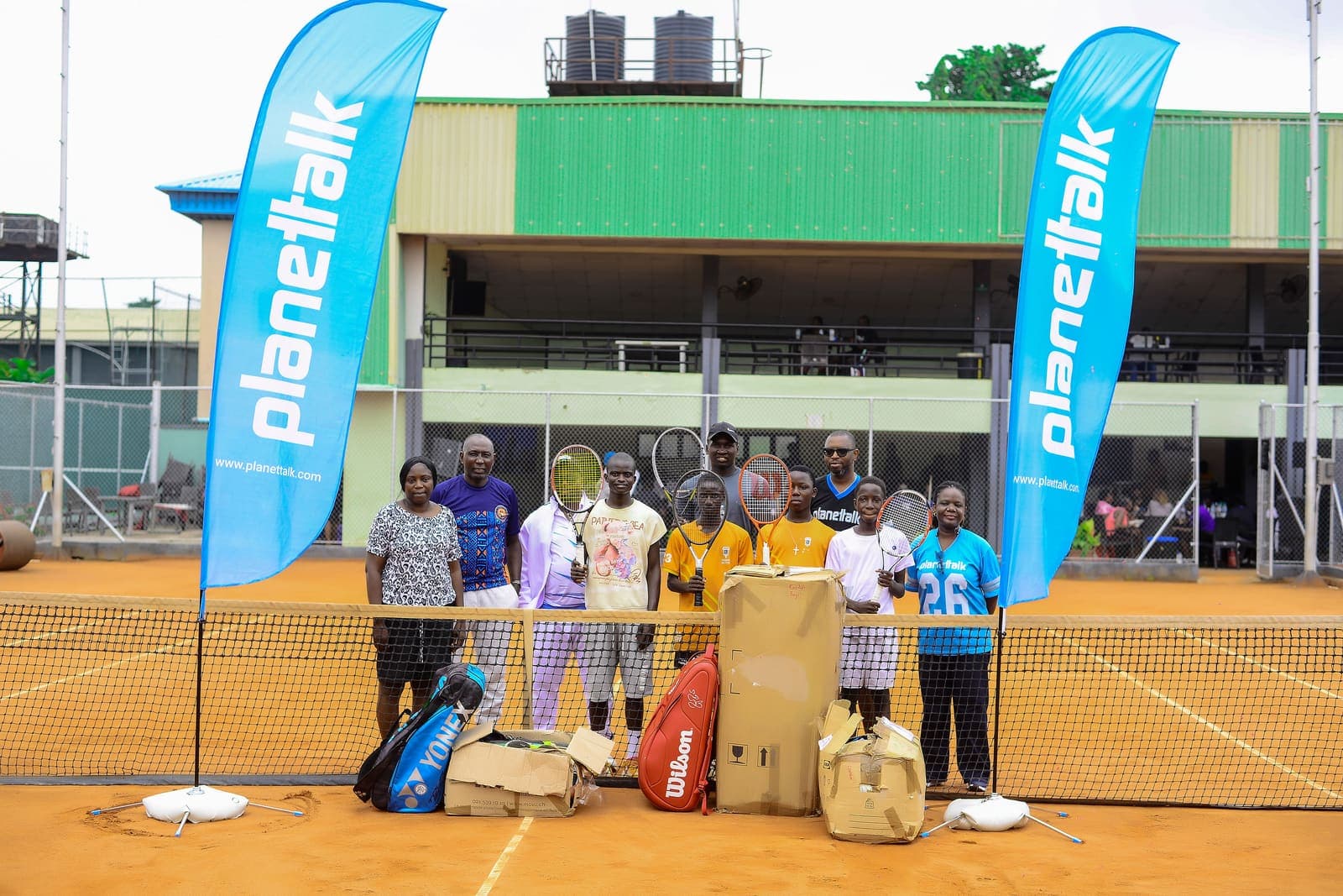 Players and organisers on the clay court in Lagos with the donated equipment between Planettalk banners